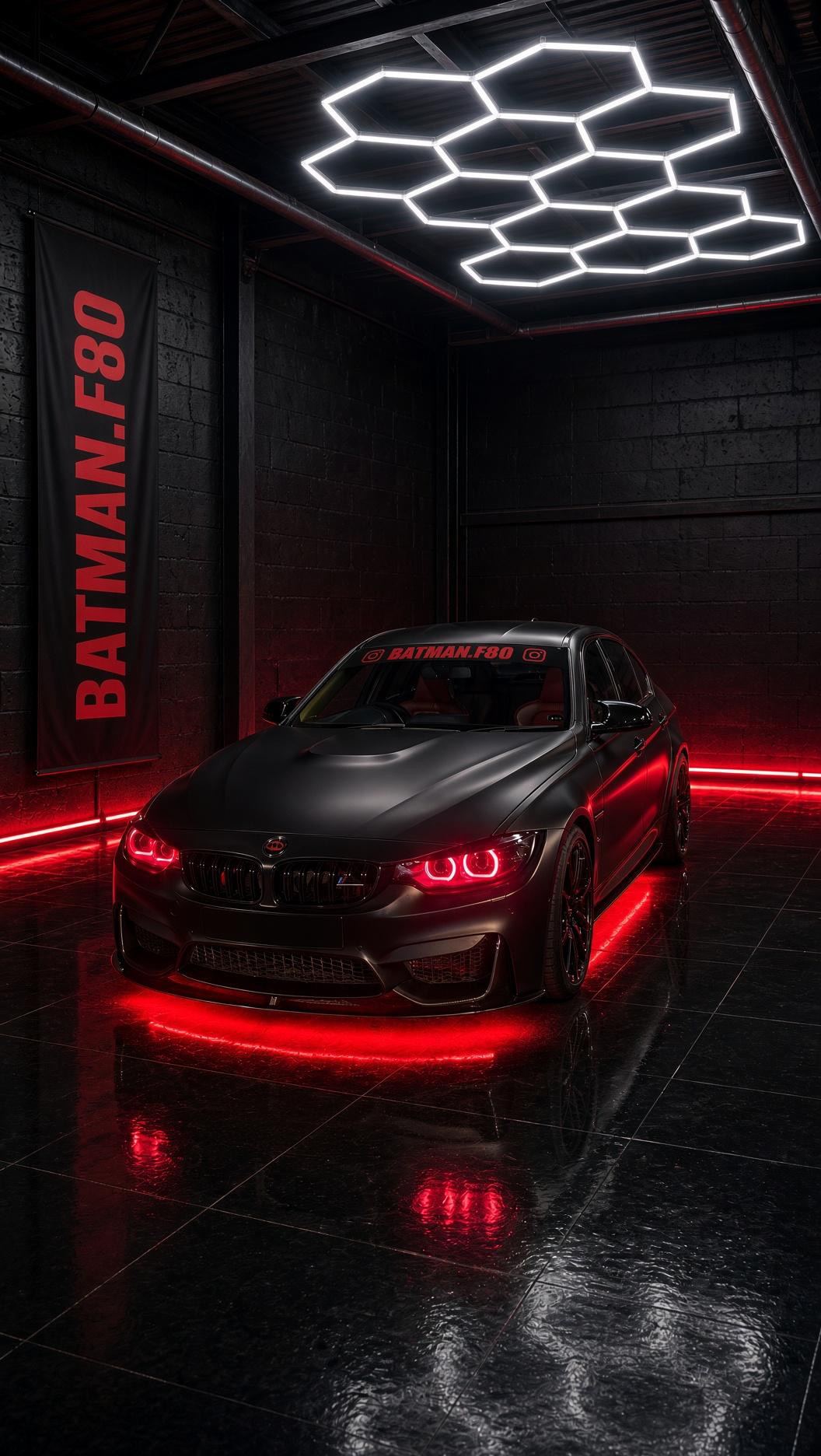 La BMW noir mat de l'atelier sous un plafonnier LED hexagonal, phares et LED sous caisse rouges allumés