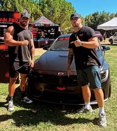 Deux hommes devant la M3 F80 noire, sur le stand de l'atelier lors d'un rassemblement